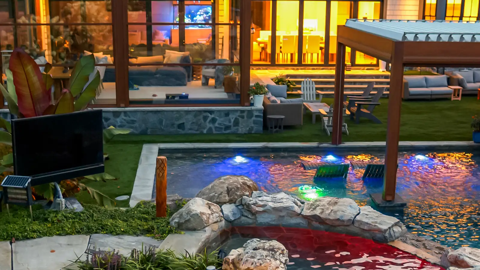 Pergola lounge and lit pool with natural boulders at dusk, built by Artisan Landscapes and Pools