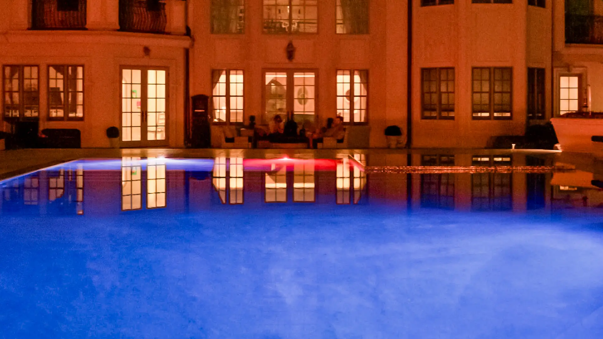 Perimeter overflow pool lit blue at night with the house windows glowing