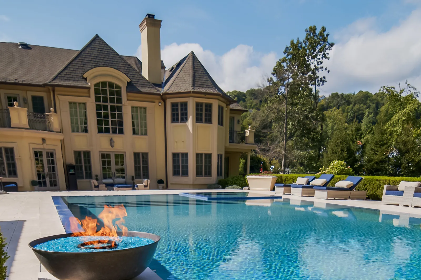 Perimeter overflow pool with an infinity edge and a fire bowl in front of the house